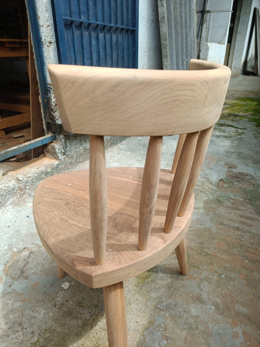 Rear view of a wooden chair with a shaped back rail and vertical spindles at the Gulmohar workshop