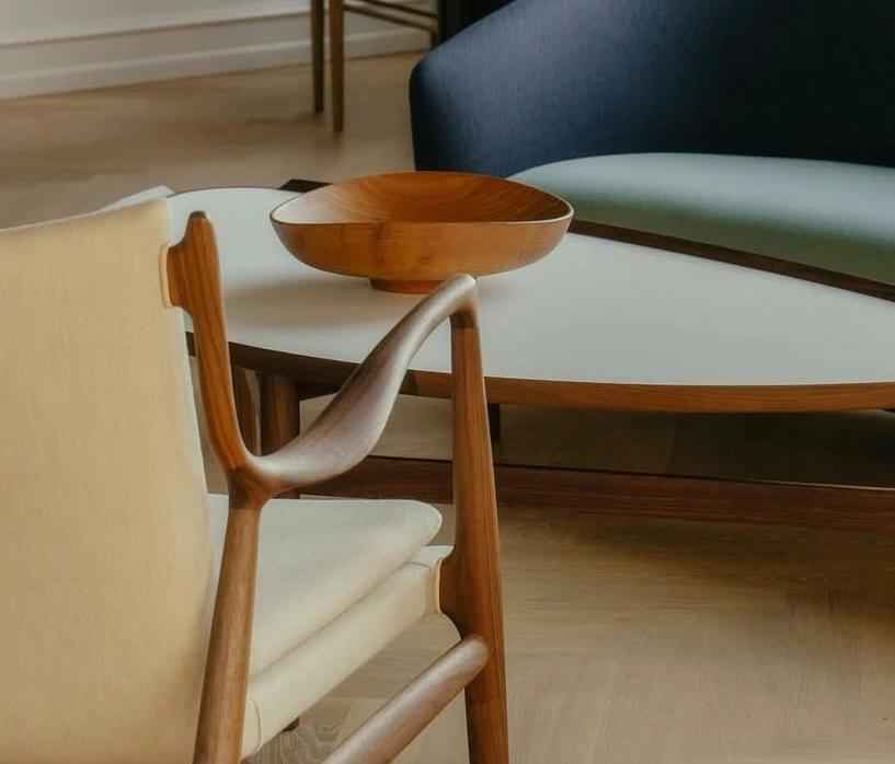 A Finn Juhl 45 Chair with a teak frame and light-colored upholstery sits near a coffee table.