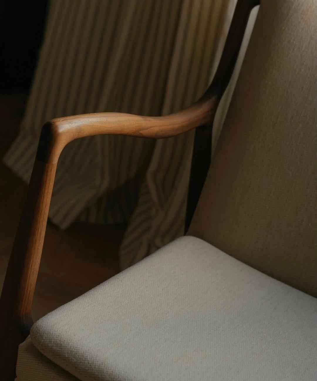 A close-up of a Finn Juhl 45 chair featuring a sculpted teak wood armrest and light upholstery.