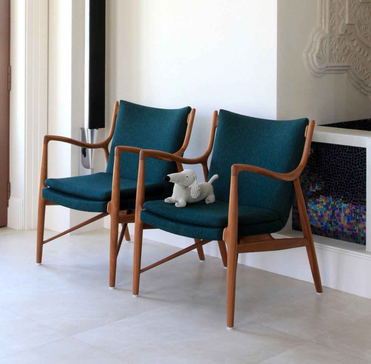 Two Finn Juhl 45 chairs with teak wood frames and dark teal upholstery sit side by side.