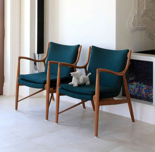 Two Finn Juhl 45 chairs with teak wood frames and dark teal upholstery sit side by side.