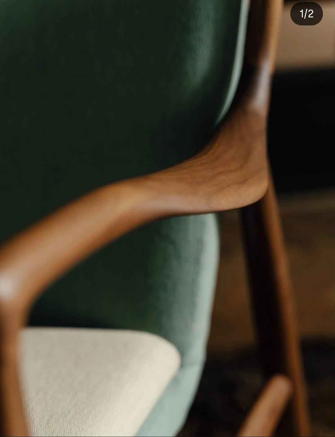 A close-up of the sculpted teak wood armrest and green upholstered back of a Finn Juhl 45 Chair.
