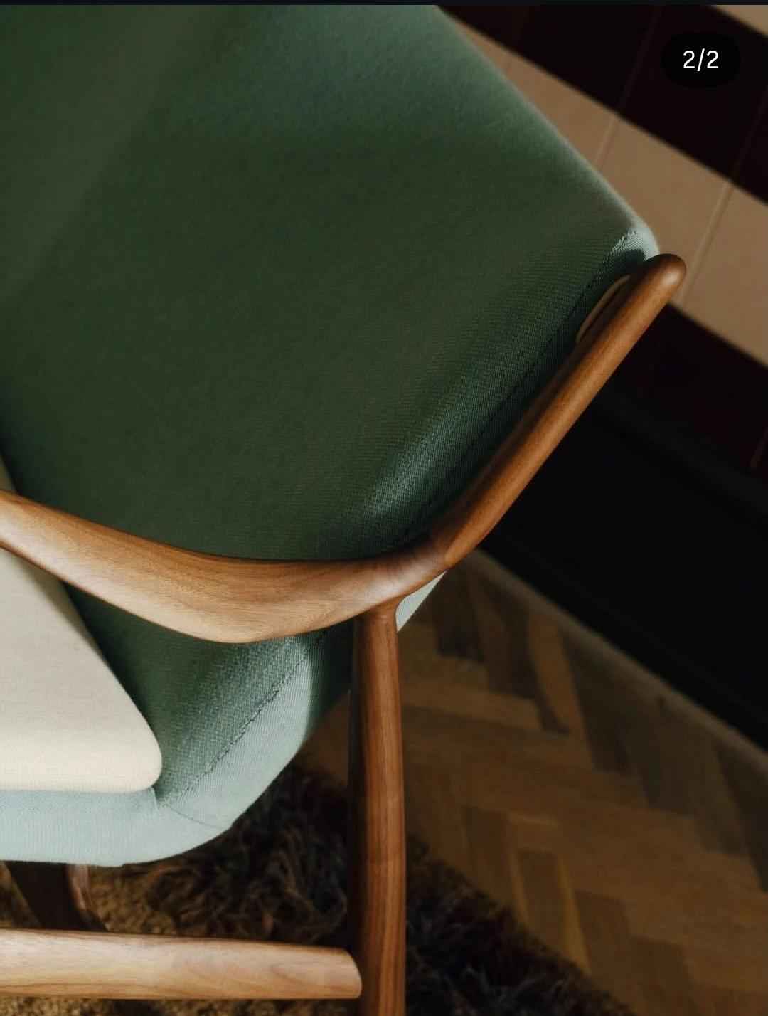 A close-up of a Finn Juhl 45 Chair featuring a green upholstered seat and a curved teak wood frame.