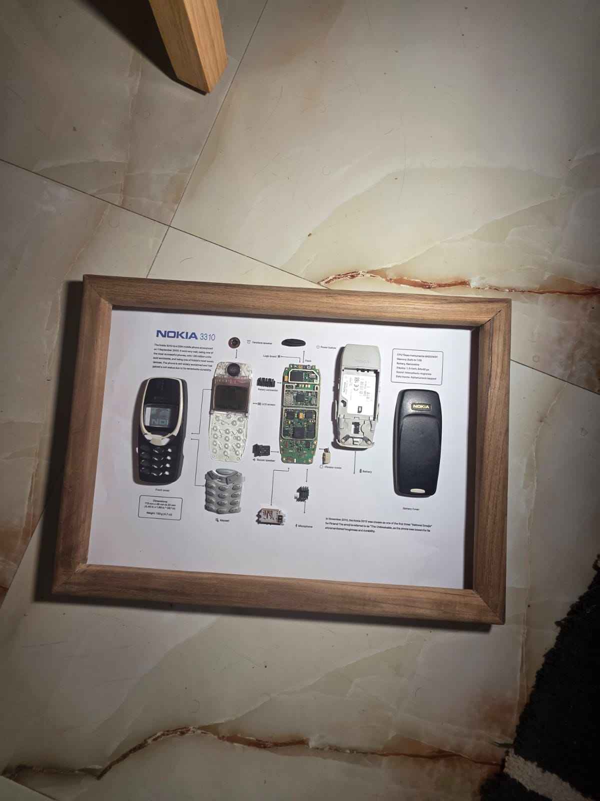A framed teardown art display featuring the disassembled components of a vintage Nokia 3310 phone.
