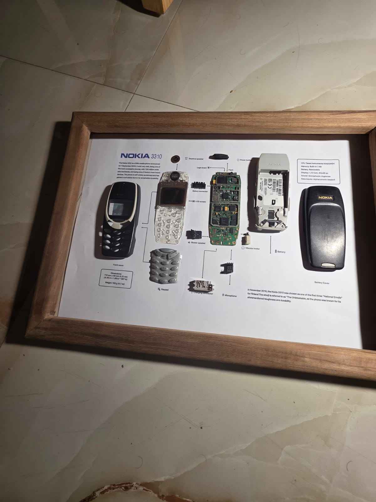 A framed teardown art display featuring the disassembled components of a vintage Nokia 3310 phone.