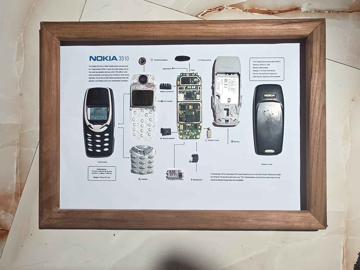 A framed teardown display of a disassembled Nokia 3310 mobile phone in a wooden frame.