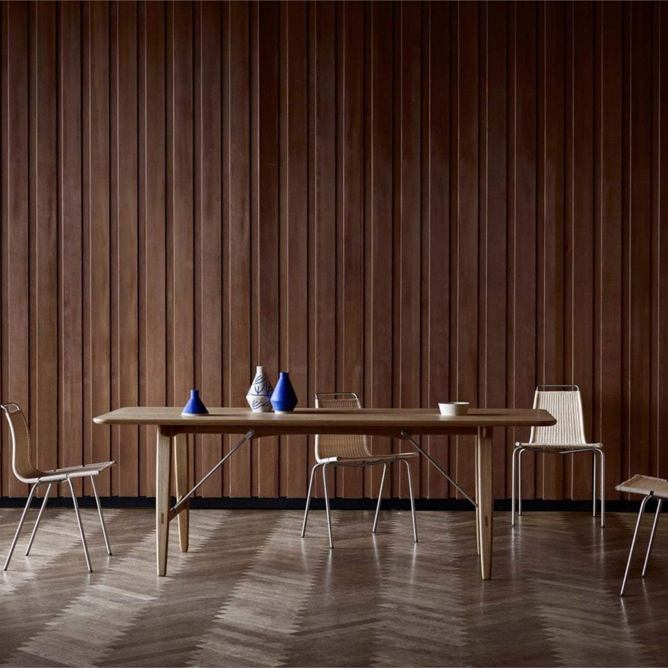 The BM1160 Hunting Table in solid wood with metal braces, surrounded by woven chairs.